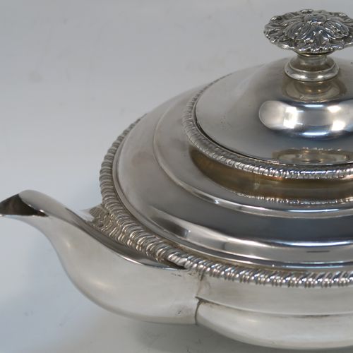 A very handsome Antique Georgian Sterling Silver teapot, having a round bellied bellied body with t applied gadroon borders, an insulated scroll handle with Anthemion leaf thumb-piece, a hinged domed lid with cast floral finial, a plain scoll spout, and all sitting on a round collet foot. This elegant silver teapot eas made by George Fox of London in 1826. The dimensions of this fine hand-made antique silver teapot are length 27.5 cms (10.75 inches), diameter of main body 18 cms (7 inches), height 12.5 cms (5 inches), and it weighs approx. 800g (25.8 troy ounces).