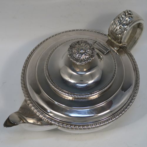 A very handsome Antique Georgian Sterling Silver teapot, having a round bellied bellied body with t applied gadroon borders, an insulated scroll handle with Anthemion leaf thumb-piece, a hinged domed lid with cast floral finial, a plain scoll spout, and all sitting on a round collet foot. This elegant silver teapot eas made by George Fox of London in 1826. The dimensions of this fine hand-made antique silver teapot are length 27.5 cms (10.75 inches), diameter of main body 18 cms (7 inches), height 12.5 cms (5 inches), and it weighs approx. 800g (25.8 troy ounces).
