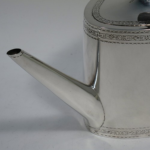 A very handsome Neoclassical style Antique Georgian Sterling Silver teapot, having an oval straight-sided body with hand-engraved upper and lower bands of floral work, with oval engraved cartouches on both sides, a straight tapering spout, a wooden scroll handle and oval finial, an invisibly hinged domed lid with matching engraving, and all sitting on a flat base. Made by William Turton of London in 1785, with a rare Incuse Duty Mark. The dimensions of this fine hand-made antique silver teapot are length 27 cms (10.5 inches), height 15 cms (6 inches), and it weighs approx. 350g (11.3 troy ounces). Please note that this item is crested.
