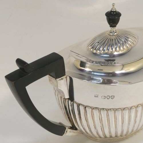 A very handsome Antique Victorian Sterling Silver teapot, having an oval body with hand-chased straight half fluting, a wooden insulated handle, a hinged domed lid with fluting, a wooden finial, and all sitting on a collet foot. This elegant antique silver teapot was made by Edward Hutton of London in 1891. The dimensions of this fine hand-made antique silver teapot are height 15 cms (6 inches), length 27.5 cms (10.75 inches), and it weighs approx. 550g (17.7 troy ounces).