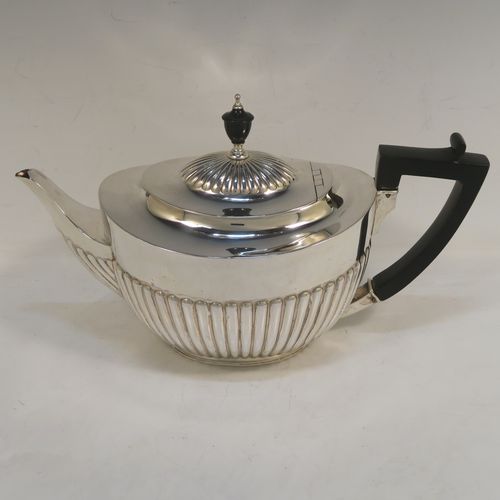 A very handsome Antique Victorian Sterling Silver teapot, having an oval body with hand-chased straight half fluting, a wooden insulated handle, a hinged domed lid with fluting, a wooden finial, and all sitting on a collet foot. This elegant antique silver teapot was made by Edward Hutton of London in 1891. The dimensions of this fine hand-made antique silver teapot are height 15 cms (6 inches), length 27.5 cms (10.75 inches), and it weighs approx. 550g (17.7 troy ounces).
