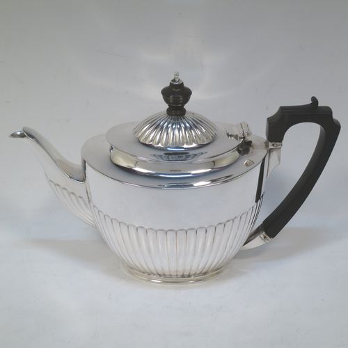 A very handsome Antique Edwardian Sterling Silver teapot, having an oval body with hand-chased straight half fluting, a wooden insulated handle, a hinged domed lid with fluting, a wooden finial, and all sitting on a collet foot. Made by Elkington and Co. Ltd., of Birmingham in 1902. The dimensions of this fine hand-made antique silver teapot are height 14.5 cms (5.75 inches), length 24 cms (9.5 inches), and it weighs is approx. 450g (14.5 troy ounces).