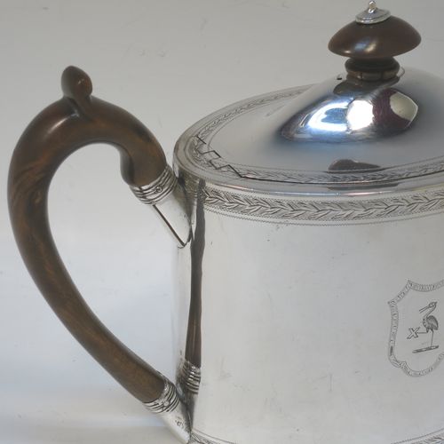 A very handsome Neoclassical style Antique Georgian Sterling Silver teapot, having an oval straight-sided body with hand-engraved upper and lower bands of floral work, with engraved cartouches on both sides, a straight tapering spout, a wooden scroll handle and oval finial, an invisibly hinged domed lid with matching engraving, and all sitting on a flat base. Made by Henry Chawner of London in 1794. The dimensions of this fine hand-made antique silver teapot are length 26 cms (10 inches), height 15 cms (6 inches), and it weighs approx. 350g (11.3 troy ounces). Please note that this item is crested.