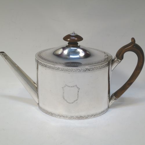 A very handsome Neoclassical style Antique Georgian Sterling Silver teapot, having an oval straight-sided body with hand-engraved upper and lower bands of floral work, with engraved cartouches on both sides, a straight tapering spout, a wooden scroll handle and oval finial, an invisibly hinged domed lid with matching engraving, and all sitting on a flat base. Made by Henry Chawner of London in 1794. The dimensions of this fine hand-made antique silver teapot are length 26 cms (10 inches), height 15 cms (6 inches), and it weighs approx. 350g (11.3 troy ounces). Please note that this item is crested.