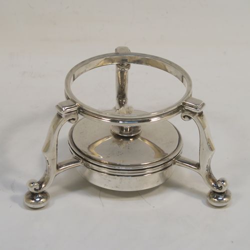 A very rare and unusual Sterling Silver bachelor sized teapot and burner stand, in a George I style with a plain round bellied body, having a hinged domed lid with wooden finial, a wooden insulated handle, a curved spout with a hinged lid, and all sitting on an original burner stand with three scroll feet and a plain round removable wick burner. This elegant silver teapot and burner stand was made by Rodney C. Pettit of London in 1981. The dimensions of this fine hand-made silver teapot and stand are height 17 cms (6.75 inches), length 17.5 cms (7 inches), and it weighs approx. 500g (16 troy ounces).