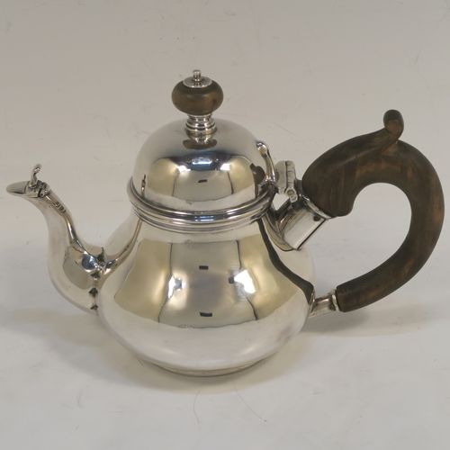 A very rare and unusual Sterling Silver bachelor sized teapot and burner stand, in a George I style with a plain round bellied body, having a hinged domed lid with wooden finial, a wooden insulated handle, a curved spout with a hinged lid, and all sitting on an original burner stand with three scroll feet and a plain round removable wick burner. This elegant silver teapot and burner stand was made by Rodney C. Pettit of London in 1981. The dimensions of this fine hand-made silver teapot and stand are height 17 cms (6.75 inches), length 17.5 cms (7 inches), and it weighs approx. 500g (16 troy ounces).