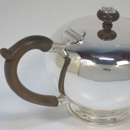 A very handsome Sterling Silver bachelor size teapot in an early George II Bullet or Skittle Ball style, having a plain round bellied body, a curved spout, a wooden scroll handle and finial with silver mount, a hinged lid, and sitting on a pedestal foot. Made by Mappin and Webb of London in 1926. The dimensions of this fine hand-made silver bachelor teapot are length 23 cms (9 inches), height 12 cms (4.75 inches), and it weighs approx. 350g (11.3 troy ounces).
