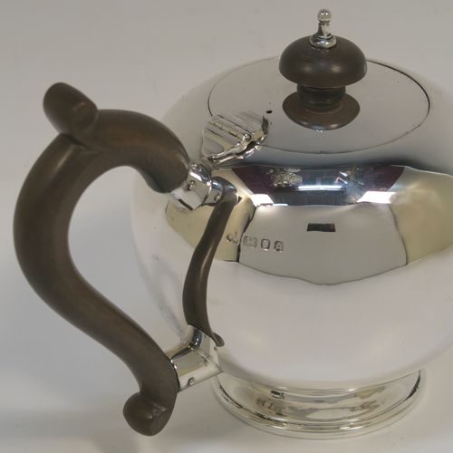 A very handsome Sterling Silver teapot in an early George II Bullet or Skittle Ball style, having a very plain round bellied body, a straight tapering spout, a wooden scroll handle and finial, a hinged flat lid, and sitting on a pedestal foot. This elegant silver teapot was made by Wakely and Wheeler of London in 1936. The dimensions of this fine hand-made silver skittle ball style teapot are length 20 cms (8 inches), height 12 cms (4.75 inches), and it weighs approx. 280g (9 troy ounces).