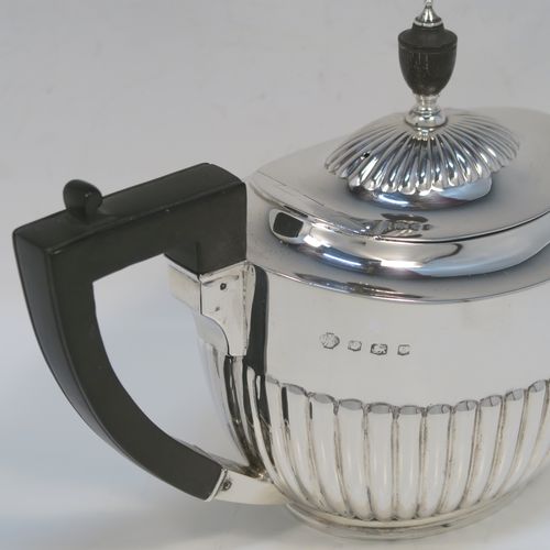 A very handsome Antique Sterling Silver teapot, having an oval body with hand-chased straight half fluting, a wooden insulated handle, a hinged domed lid with fluting, a wooden finial, and all sitting on a collet foot. This elegant silver teapot was made by William Hutton and Sons of Sheffield in 1926. The dimensions of this fine hand-made antique silver teapot are height 14.5 cms (5.75 inches), length 26 cms (10.25 inches), and it weighs is approx. 450g (14.5 troy ounces).