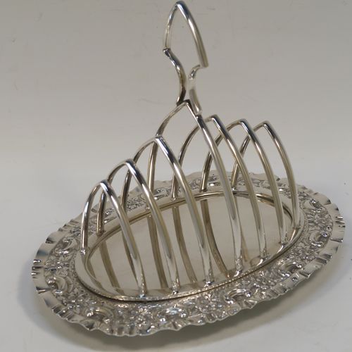 A very pretty Antique Victorian Silver Plated seven-bar toast-rack, having seven arch-shaped and graduated wire-work toast holders, attached to a crumb plate with a hand-chased scroll and floral decorated border, and all sitting on four ball feet. This beautiful antique toastrack was made by Joseph Rogers of Sheffield in ca. 1880. The dimensions of this fine hand-made antique silver-plated toast-rack are length 18 cms (7 inches), height 15 cms (6 inches), and width 13 cms (5 inches).