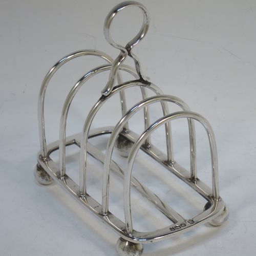 A handsome Sterling Silver five-bar toastrack, having plain rounded wire-work bars, a matching loop handle, all sitting on a rectangular base with a strengthening strut, on four cast ball feet. Made by Thomas Bradbury of Sheffield in 1924. The dimensions of this fine hand-made silver toast-rack are length 11.5 cms (4.5 inches), height 11.5 cms (4.5 inches), width 7 cms (2.75 inches), and it weighs approx. 175g (5.6 troy ounces).  