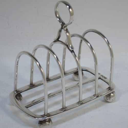 A handsome Sterling Silver five-bar toastrack, having plain rounded wire-work bars, a matching loop handle, all sitting on a rectangular base with a strengthening strut, on four cast ball feet. Made by Thomas Bradbury of Sheffield in 1924. The dimensions of this fine hand-made silver toast-rack are length 11.5 cms (4.5 inches), height 11.5 cms (4.5 inches), width 7 cms (2.75 inches), and it weighs approx. 175g (5.6 troy ounces).