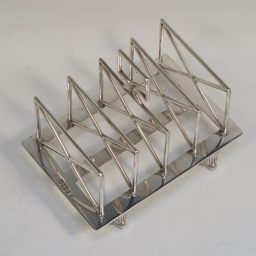A very unusual Arts and Crafts style Antique Victorian Sterling Silver five-bar toastrack, having square crossed wire-work bars, with a square loop handle, and sitting on a base with a strengthening strut and four fluted and flanged feet. This elegant Arts and Crafts silver toast-rack was made by Edward Hutton of London in 1881. The dimensions of this fine hand-made antique silver toast-rack are length 12.5 cms (5 inches), height 11 cms (4.3 inches), width 9 cms (3.5 inches), and it weighs approx. 259g (8.4 troy ounces).