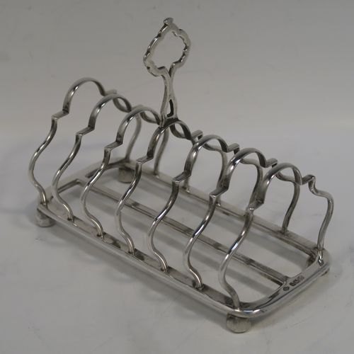 A pretty Antique Sterling Silver seven-bar toastrack, having plain shaped and lobed cross-section wire-work bars, a matching loop handle, and all sitting on a rectangular base with a strengthening strut and four ball feet. This handsome antique silver toast-rack was made by William Hutton of Sheffield in 1912. The dimensions of this fine hand-made antique silver toast-rack are length 16.5 cms (6.5 inches), height 12.5 cms (5 inches), width 8.5 cms (3.3 inches), and it weighs approx. 265g (8.5 troy ounces).   