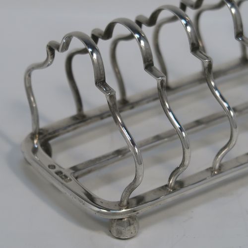 A pretty Antique Sterling Silver seven-bar toastrack, having plain shaped and lobed cross-section wire-work bars, a matching loop handle, and all sitting on a rectangular base with a strengthening strut and four ball feet. This handsome antique silver toast-rack was made by William Hutton of Sheffield in 1912. The dimensions of this fine hand-made antique silver toast-rack are length 16.5 cms (6.5 inches), height 12.5 cms (5 inches), width 8.5 cms (3.3 inches), and it weighs approx. 265g (8.5 troy ounces).