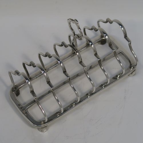 A pretty Antique Sterling Silver seven-bar toastrack, having plain shaped and lobed cross-section wire-work bars, a matching loop handle, and all sitting on a rectangular base with a strengthening strut and four ball feet. This handsome antique silver toast-rack was made by William Hutton of Sheffield in 1912. The dimensions of this fine hand-made antique silver toast-rack are length 16.5 cms (6.5 inches), height 12.5 cms (5 inches), width 8.5 cms (3.3 inches), and it weighs approx. 265g (8.5 troy ounces).