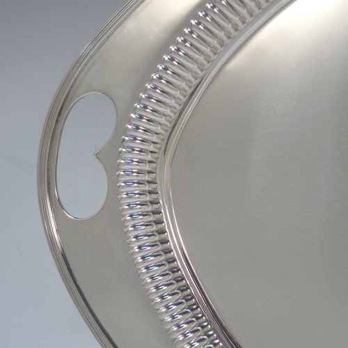 A very pretty Antique Victorian Sterling Silver oval two-handled tea tray, having a plain ground, with straight-fluted border and applied reeded edge, all sitting on a flat base. This very handsome silver tray was made by James Walter Deakin of Sheffield in 1892. The dimensions of this fine hand-made silver tray are length 46 cms (18 inches), width 32 cms (12.5 inches), and it weighs approx. 1,125g (36.3 troy ounces).
