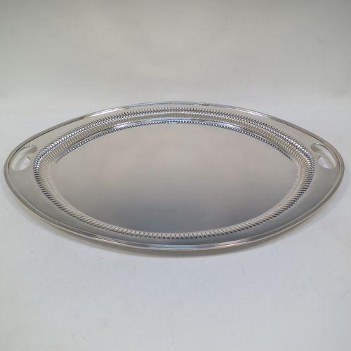 A very pretty Antique Victorian Sterling Silver oval two-handled tea tray, having a plain ground, with straight-fluted border and applied reeded edge, all sitting on a flat base. This very handsome silver tray was made by James Walter Deakin of Sheffield in 1892. The dimensions of this fine hand-made silver tray are length 46 cms (18 inches), width 32 cms (12.5 inches), and it weighs approx. 1,125g (36.3 troy ounces).