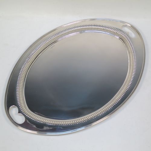 A very pretty Antique Victorian Sterling Silver oval two-handled tea tray, having a plain ground, with straight-fluted border and applied reeded edge, all sitting on a flat base. This very handsome silver tray was made by James Walter Deakin of Sheffield in 1892. The dimensions of this fine hand-made silver tray are length 46 cms (18 inches), width 32 cms (12.5 inches), and it weighs approx. 1,125g (36.3 troy ounces).