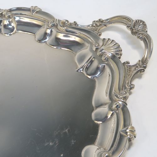 A very elegant Antique Edwardian Sterling Silver tray, having a shaped oval body with a plain ground, an applied shell and scroll border, and two cast side-handles, all sitting on a flat base. This classical silver tray was made by George Howson of Sheffield in 1902. The dimensions of this fine hand-made antique silver tray are length (inc. handles) 74 cms (29 inches), width 48 cms (19 inches), and it weighs approx. 3,510g (117 troy ounces).