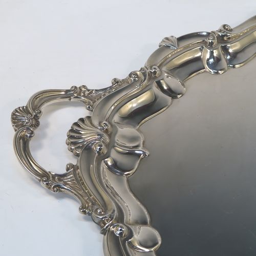 A very elegant Antique Edwardian Sterling Silver tray, having a shaped oval body with a plain ground, an applied shell and scroll border, and two cast side-handles, all sitting on a flat base. This classical silver tray was made by George Howson of Sheffield in 1902. The dimensions of this fine hand-made antique silver tray are length (inc. handles) 74 cms (29 inches), width 48 cms (19 inches), and it weighs approx. 3,510g (117 troy ounces).