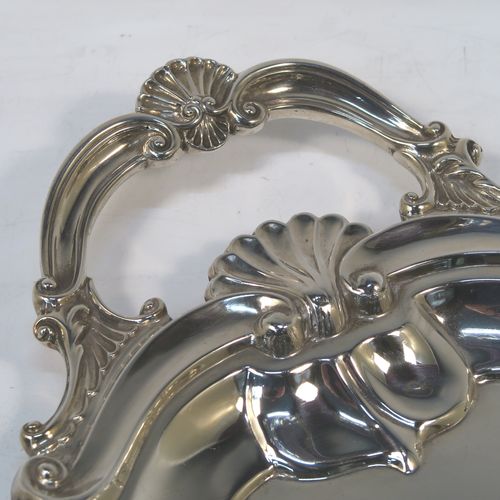A very elegant Antique Edwardian Sterling Silver tray, having a shaped oval body with a plain ground, an applied shell and scroll border, and two cast side-handles, all sitting on a flat base. This classical silver tray was made by George Howson of Sheffield in 1902. The dimensions of this fine hand-made antique silver tray are length (inc. handles) 74 cms (29 inches), width 48 cms (19 inches), and it weighs approx. 3,510g (117 troy ounces).