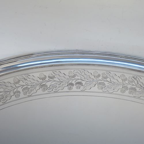 A very elegant Antique Georgian Sterling Silver tray, having an oval body with a plain central ground surrounded by a band of hand-engraved acorn and oak leaf decoration, with an applied reeded border, and two cast reeded handles, all sitting on four cast flange feet. This beautiful antique silver tray was made by Peter, Anne, and William Bateman of London in 1802. The dimensions of this fine hand-made antique silver tray are length (inc. handles) 55 cms (21.75 inches), width 35.5 cms (14 inches), height 4.5 cms (1.75 inches), and it weighs approx. 1,795g (58 troy ounces).
