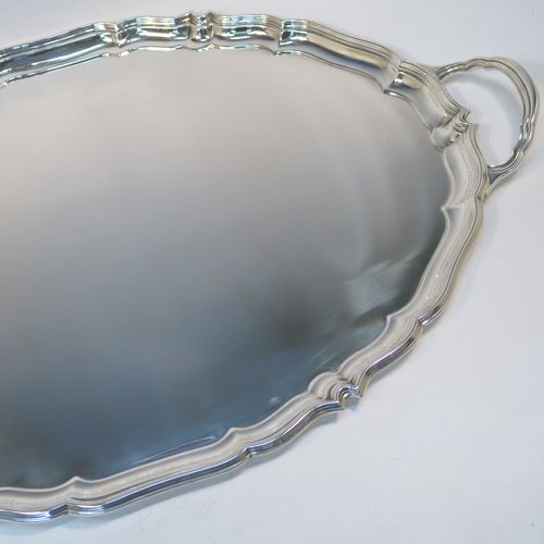 A very handsome Sterling Silver oval two-handled tea tray, having a plain ground, with an applied Chippendale border, two cast side handles, and all sitting on a flat base. This elegant silver tray was made by Harrison Brothers and Howson of Sheffield in 1928. The dimensions of this fine hand-made sterling silver tray are length (inc. handles) 70 cms (27.5 inches), width 43 cms (17 inches), and it weighs approx. 3,100g (100 troy ounces).