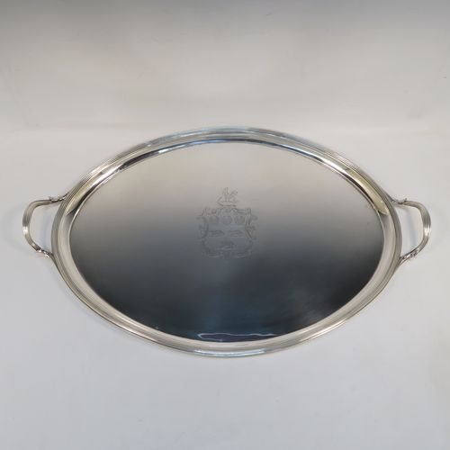 A very elegant Antique Georgian Sterling Silver oval two-handled tea tray, having a plain ground with a hand-engraved full armorial crest, an applied Reeded border, two cast reeded side handles, and all sitting on a flat base. This very handsome antique silver tray was made by Elizabeth Jones of London in 1794. The dimensions of this fine hand-made antique silver tray are length (inc. handles) 56 cms (22 inches), width 36 cms (14.25 inches), and it weighs approx. 1,923g (62 troy ounces).   