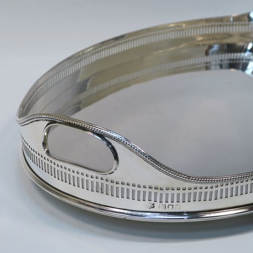 A very handsome Antique Victorian Sterling Silver galleried drinks tray, having an oval body with a hand-pierced gallery, with two oval cut-out side-handles, an applied bead-edged top border, a plain oval ground, and sitting on four cast ball feet. This elegant antique silver drinks tray was made by John Newton Mappin of London in 1896. The dimensions of this fine hand-made silver gallery tray are length 39 cms (15.3 inches), width 26.5 cms (10.5 inches), and it weighs approx. 1,115g (36 troy ounces).