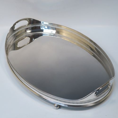 A very handsome Antique Victorian Sterling Silver galleried drinks tray, having an oval body with a hand-pierced gallery, with two oval cut-out side-handles, an applied bead-edged top border, a plain oval ground, and sitting on four cast ball feet. This elegant antique silver drinks tray was made by John Newton Mappin of London in 1896. The dimensions of this fine hand-made silver gallery tray are length 39 cms (15.3 inches), width 26.5 cms (10.5 inches), and it weighs approx. 1,115g (36 troy ounces).