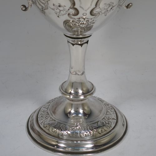 A very beautiful Antique Victorian Sterling Silver trophy cup, having a round body with tapering sides all hand-chased with floral and scroll decoration surrounding vacant cartouches either side, two cast scroll handles with figural thumb-pieces, a gold-gilt interior, and all sitting on a pedestal foot. Made by John Edward Bingham and Charles Henry Bingham of Sheffield in 1876. The dimensions of this fine hand-made antique silver trophy cup are height 24 cms (9.5 inches), spread across arms 22 cms (8.75 inches), and it weighs approx. 620g (20 troy ounces).