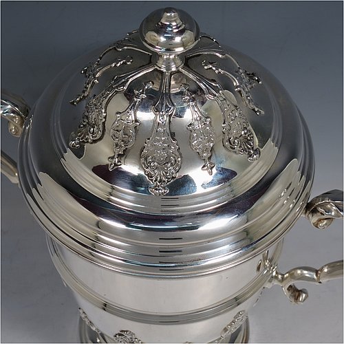 A Sterling Silver trophy cup and cover, in a George II style, having a round body with applied floral strap-work decoration, two scroll side-handles with anthemion leaf thumb-pieces, a central applied girdle band, a pull-off lid with matching applied strap-work and a cast round finial, and all sitting on a stepped pedestal foot. Made by George Bryan & Co., of Birmingham in 1936. The dimensions of this fine hand-made silver trophy cup and cover are height 30 cms (11.75 inches), spread across arms 26.5 cms (10.5 inches), and it weighs approx. 1,132g (36.5 troy ounces).