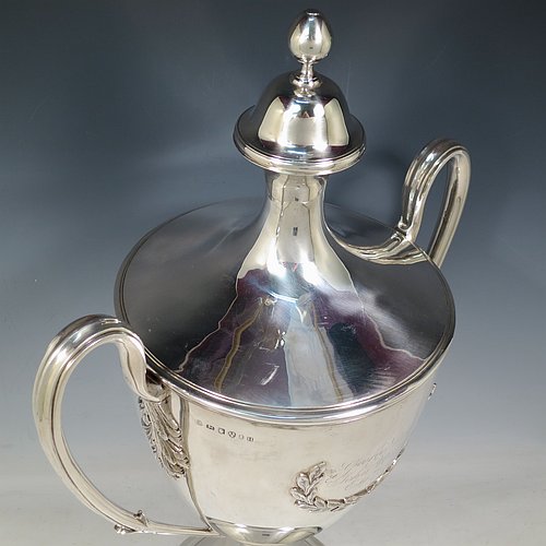 A rare Antique Georgian Sterling Silver large trophy cup and cover, having a neoclassical round plain tapering body with applied laurel-leaf cartouches, with applied reeded borders, two loop side-handles with anthemion leaf shoulders, an original cover with cast finial, and sitting on a round pedestal foot. Made by John Langland II of Newcastle in 1798. The dimensions of this fine hand-made antique silver trophy cup and cover are height 51 cms (20 inches), spread across arms 33 cms (13 inches), and it weighs approx. 3,176g (102 troy ounces). Please note that this trophy is engraved with contemporary presentation inscriptions on both sides.