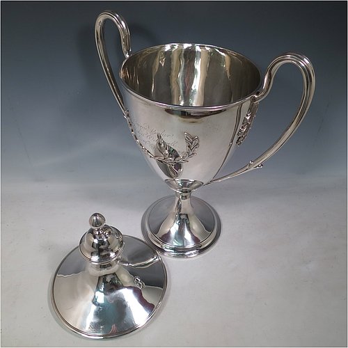 A rare Antique Georgian Sterling Silver large trophy cup and cover, having a neoclassical round plain tapering body with applied laurel-leaf cartouches, with applied reeded borders, two loop side-handles with anthemion leaf shoulders, an original cover with cast finial, and sitting on a round pedestal foot. Made by John Langland II of Newcastle in 1798. The dimensions of this fine hand-made antique silver trophy cup and cover are height 51 cms (20 inches), spread across arms 33 cms (13 inches), and it weighs approx. 3,176g (102 troy ounces). Please note that this trophy is engraved with contemporary presentation inscriptions on both sides.
