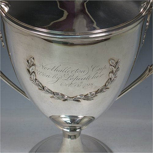 A rare Antique Georgian Sterling Silver large trophy cup and cover, having a neoclassical round plain tapering body with applied laurel-leaf cartouches, with applied reeded borders, two loop side-handles with anthemion leaf shoulders, an original cover with cast finial, and sitting on a round pedestal foot. Made by John Langland II of Newcastle in 1798. The dimensions of this fine hand-made antique silver trophy cup and cover are height 51 cms (20 inches), spread across arms 33 cms (13 inches), and it weighs approx. 3,176g (102 troy ounces). Please note that this trophy is engraved with contemporary presentation inscriptions on both sides.