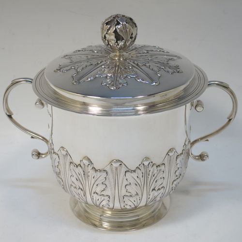 A very handsome Antique Sterling Silver trophy cup and cover, in the shape of a lidded Porringer, having a round body with hand-chased Anthemion leaf decoration, with two scroll side-handles, a lift-off cover with matching decoration and a pierced floral finial, and all sitting on a stepped pedestal foot. This elegant antique silver trophy cup and cover was made by Charles Stuart Harris of London in 1925. The dimensions of this fine hand-made antique silver trophy cup and cover are height 18 cms (7 inches), spread across handles 21 cms (8.25 inches), and it weighs approx. 748g (24 troy ounces).   