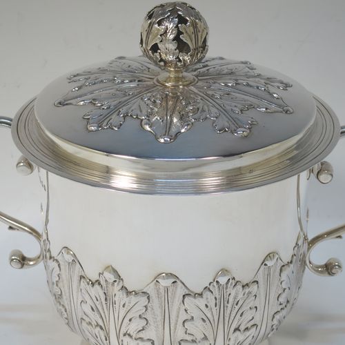A very handsome Antique Sterling Silver trophy cup and cover, in the shape of a lidded Porringer, having a round body with hand-chased Anthemion leaf decoration, with two scroll side-handles, a lift-off cover with matching decoration and a pierced floral finial, and all sitting on a stepped pedestal foot. This elegant antique silver trophy cup and cover was made by Charles Stuart Harris of London in 1925. The dimensions of this fine hand-made antique silver trophy cup and cover are height 18 cms (7 inches), spread across handles 21 cms (8.25 inches), and it weighs approx. 748g (24 troy ounces).