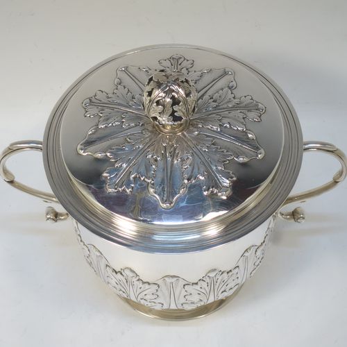 A very handsome Antique Sterling Silver trophy cup and cover, in the shape of a lidded Porringer, having a round body with hand-chased Anthemion leaf decoration, with two scroll side-handles, a lift-off cover with matching decoration and a pierced floral finial, and all sitting on a stepped pedestal foot. This elegant antique silver trophy cup and cover was made by Charles Stuart Harris of London in 1925. The dimensions of this fine hand-made antique silver trophy cup and cover are height 18 cms (7 inches), spread across handles 21 cms (8.25 inches), and it weighs approx. 748g (24 troy ounces).