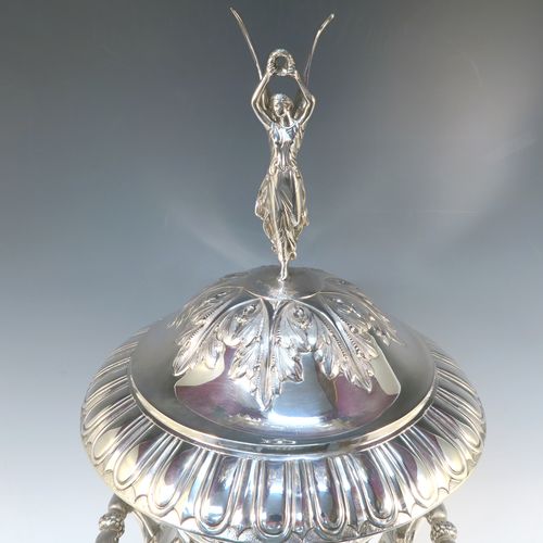 A very handsome and large Antique Edwardian Sterling Silver trophy cup and cover, having a Campana style round bellied body with hand-chased floral, scroll, and fluted decoration, with two cast side handles, and sitting on a pedestal foot. The pull-off cover with matching decoration and a cast figural finial of the goddess Nike. This beautiful and impressive antique silver trophy cup and cover was made by Jay, Richard Attenborough and Co., of London in 1910. The dimensions of this fine hand-made antique silver trophy cup are height 66 cms (26 inches), spread across handles 29 cms (11.5 inches), and it weighs approx. 3,670g (118 troy ounces).