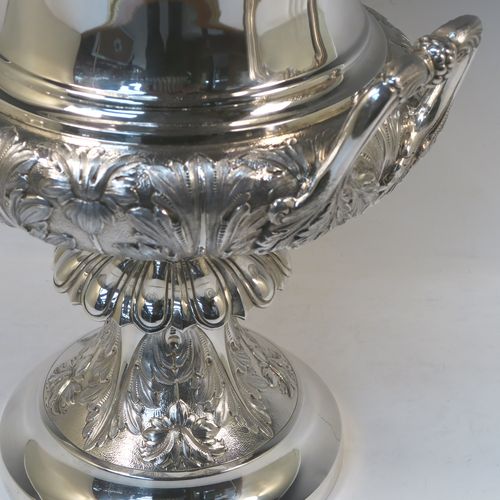 A very handsome and large Antique Edwardian Sterling Silver trophy cup and cover, having a Campana style round bellied body with hand-chased floral, scroll, and fluted decoration, with two cast side handles, and sitting on a pedestal foot. The pull-off cover with matching decoration and a cast figural finial of the goddess Nike. This beautiful and impressive antique silver trophy cup and cover was made by Jay, Richard Attenborough and Co., of London in 1910. The dimensions of this fine hand-made antique silver trophy cup are height 66 cms (26 inches), spread across handles 29 cms (11.5 inches), and it weighs approx. 3,670g (118 troy ounces).