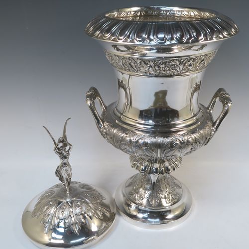 A very handsome and large Antique Edwardian Sterling Silver trophy cup and cover, having a Campana style round bellied body with hand-chased floral, scroll, and fluted decoration, with two cast side handles, and sitting on a pedestal foot. The pull-off cover with matching decoration and a cast figural finial of the goddess Nike. This beautiful and impressive antique silver trophy cup and cover was made by Jay, Richard Attenborough and Co., of London in 1910. The dimensions of this fine hand-made antique silver trophy cup are height 66 cms (26 inches), spread across handles 29 cms (11.5 inches), and it weighs approx. 3,670g (118 troy ounces).