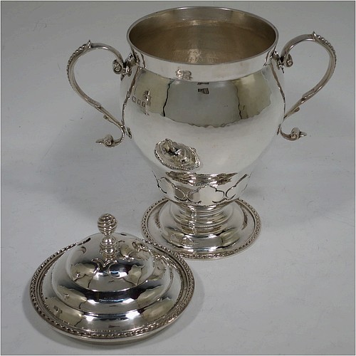 A very unusual pair of Sterling Silver trophy cups and covers, in an Arts and Crafts style, having round bellied bodies with hand-hammered decoration, applied zigzag borders and cut-card work, two side scroll handles with beaded thumb-pieces, removable covers with spiral finials, and all sitting on stepped pedestal feet. Made by D. and J. Wellby of London in 1931. The dimensions of these fine hand-made silver trophy cups and covers are height 17.5 cms (7 inches), spread across arms 15 cms (6 inches), and they weigh a total of approx. 825g (26.6 troy ounces).
