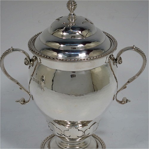 A very unusual pair of Sterling Silver trophy cups and covers, in an Arts and Crafts style, having round bellied bodies with hand-hammered decoration, applied zigzag borders and cut-card work, two side scroll handles with beaded thumb-pieces, removable covers with spiral finials, and all sitting on stepped pedestal feet. Made by D. and J. Wellby of London in 1931. The dimensions of these fine hand-made silver trophy cups and covers are height 17.5 cms (7 inches), spread across arms 15 cms (6 inches), and they weigh a total of approx. 825g (26.6 troy ounces).