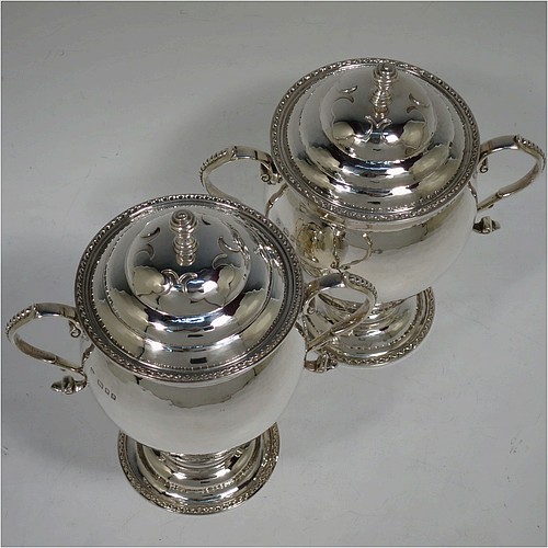 A very unusual pair of Sterling Silver trophy cups and covers, in an Arts and Crafts style, having round bellied bodies with hand-hammered decoration, applied zigzag borders and cut-card work, two side scroll handles with beaded thumb-pieces, removable covers with spiral finials, and all sitting on stepped pedestal feet. Made by D. and J. Wellby of London in 1931. The dimensions of these fine hand-made silver trophy cups and covers are height 17.5 cms (7 inches), spread across arms 15 cms (6 inches), and they weigh a total of approx. 825g (26.6 troy ounces).