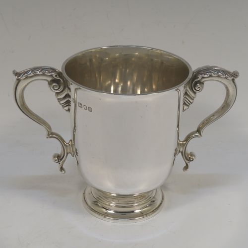 A very handsome and heavy Sterling Silver trophy cup in a George III neoclassical style, having a plain round body with tapering sides, two cast scroll side-handles with anthemion leaf decoration, and all sitting on a stepped pedestal foot. This beautiful sterling silver trophy cup was made by D. and J. Welby of London in 1938. The dimensions of this fine hand-made silver trophy cup are height 12.5 cms (5 inches), spread across arms 18 cms (7 inches), and it weighs approx. 414g (13.4 troy ounces).  