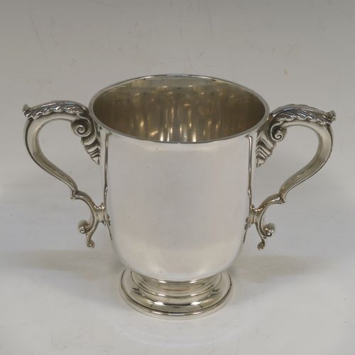 A very handsome and heavy Sterling Silver trophy cup in a George III neoclassical style, having a plain round body with tapering sides, two cast scroll side-handles with anthemion leaf decoration, and all sitting on a stepped pedestal foot. This beautiful sterling silver trophy cup was made by D. and J. Welby of London in 1938. The dimensions of this fine hand-made silver trophy cup are height 12.5 cms (5 inches), spread across arms 18 cms (7 inches), and it weighs approx. 414g (13.4 troy ounces).