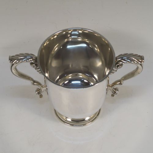 A very handsome and heavy Sterling Silver trophy cup in a George III neoclassical style, having a plain round body with tapering sides, two cast scroll side-handles with anthemion leaf decoration, and all sitting on a stepped pedestal foot. This beautiful sterling silver trophy cup was made by D. and J. Welby of London in 1938. The dimensions of this fine hand-made silver trophy cup are height 12.5 cms (5 inches), spread across arms 18 cms (7 inches), and it weighs approx. 414g (13.4 troy ounces).