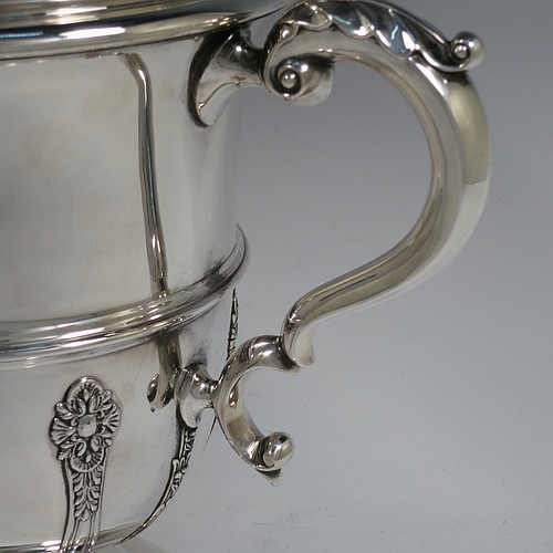 A very handsome Antique Edwardian Sterling Silver trophy cup and cover, in a George II style, having a round body with applied floral strap-work decoration, two scroll side-handles with anthemion leaf thumb-pieces, a central applied girdle band, a pull-off lid with matching applied strap-work and a cast round floral finial, and all sitting on a stepped pedestal foot. Made by Walker and Hall of Sheffield in 1909. The dimensions of this fine hand-made antique silver trophy cup and cover are height 37 cms (14.5 inches), spread across arms 33 cms (13 inches), and it weighs approx. 1,570g (51 troy ounces).