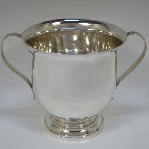 A handsome Sterling Silver trophy cup, having a plain round bellied body, two side-handles with reeded decoration, and sitting on a round stepped pedestal foot. Made by Henry Wilkinson of Sheffield in 1921. The dimensions of this fine hand-made silver trophy cup and are height 15 cms (6 inches), spread across arms 21 cms (8.25 inches), and it weighs approx. 504g (16 troy ounces).   